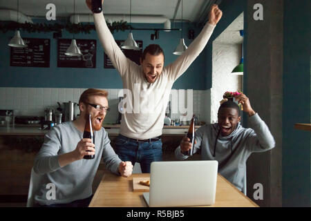 Heureux les gars millénaire célébrant la victoire de regarder match de football sur ordinateur portable en pub, divers hommes crier appuyer les sports team objectif de notation, drinki Banque D'Images