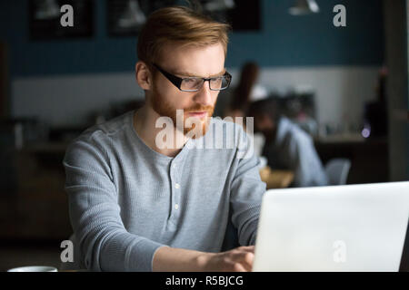 Homme aux cheveux rouge graves au travail laptop sitting in cafe, porté à l'étude d'étudiant millénaire ordinateur, occupé à internet navigation coffeeshop, concentrat Banque D'Images