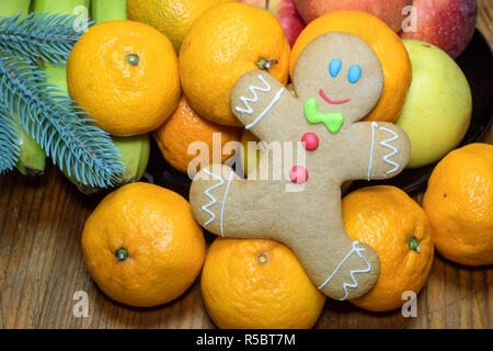 D'épices faits maison de Noël sous la forme d'un petit homme sur une table de bois parmi les fruits tropicaux. Close-up. Banque D'Images
