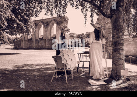 Deux jeunes femmes en costumes d'époque édouardienne posent avec leur chevalet sur un jour d'été à l'abbaye historique à Glastonbury, dans le Somerset. Banque D'Images