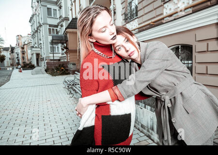 Serrant sa sœur. Red-haired woman hugging élégant sa belle soeur aux cheveux blonds en dehors de la rue Banque D'Images