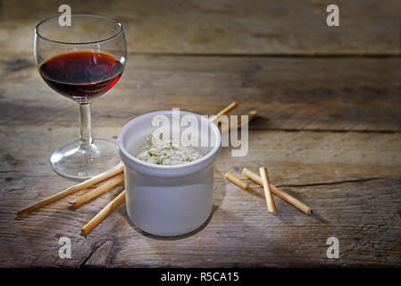 Le fromage stilton bleu en pot dans un pot en céramique, du vin et quelques bâtonnets de grignoter sur une table en bois rustique, de copie, de l'espace, la profondeur de mise au point sélectionnée étroit Banque D'Images