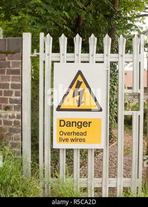 Un signe de sécurité électrique à l'extérieur sur la porte de métal avec vis électrique dans le triangle jaune et noir danger live wires overhead Banque D'Images