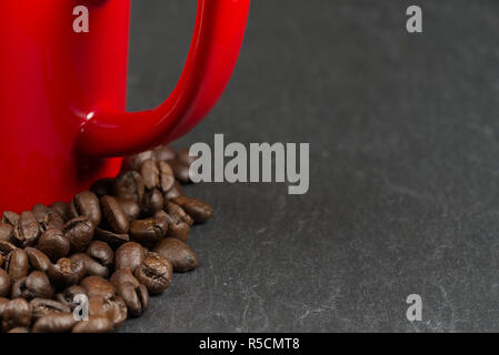 Café en grains entourant une tasse rouge sur un fond d'ardoise avec une faible profondeur de champ. Aime le café concept Banque D'Images