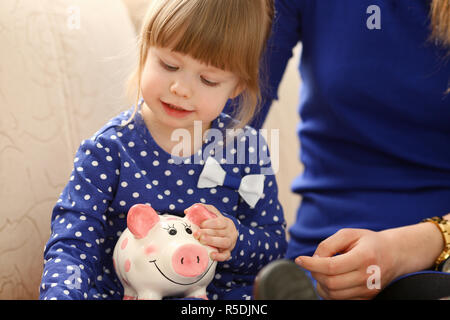 Le bras de l'enfant petite fille mettre des pièces en piggybank Banque D'Images