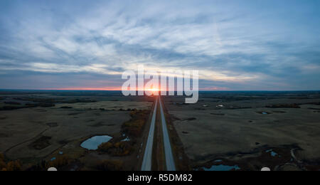 Vue Aérienne Vue panoramique de la route dans les Prairies au cours d'une vibrante nuageux coucher du soleil. Pris à l'est d'Edmonton, Alberta, Canada. Banque D'Images