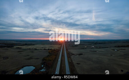 Vue Aérienne Vue panoramique de la route dans les Prairies au cours d'une vibrante nuageux coucher du soleil. Pris à l'est d'Edmonton, Alberta, Canada. Banque D'Images