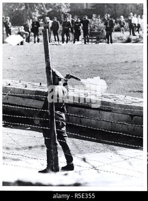 Octobre 1961 - 'communiste' (policiers du peuple Volkspolizist), Comité permanent entre la frontière et le mur, se prépare à lancer une Tear-Gas Grenade sur un groupe de Berlinois de l'Ouest qui se sont réunis de leur côté de la frontière pour se moquer les Gardes Rouges Banque D'Images