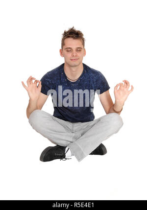 Un beau jeune homme en jeans gris assis sur le plancher avec ses yeux fermés et les mains en faisant du yoga, isolée pour fond blanc Banque D'Images