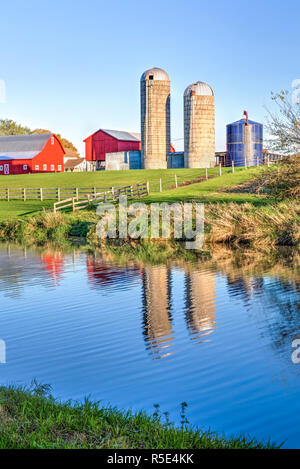 Lever tôt le matin les bougies s'allume une ferme avec des granges et des silos rouges se reflétant dans les eaux de l'Illinois' Apple River. Banque D'Images