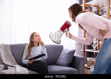 Mère crier par mégaphone à Careless Girl Sitting on Sofa Using Digital Tablet Banque D'Images