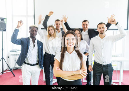 Jeune femme blanche directrice debout devant des collègues avec leurs bras levés. Banque D'Images