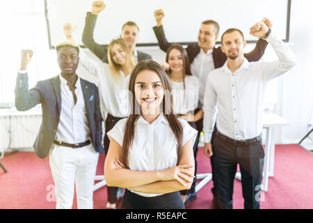 Jeune femme blanche directrice debout devant des collègues avec leurs bras levés. Banque D'Images