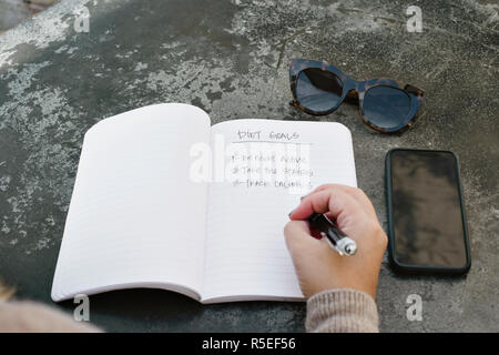 Une jeune femme écrit son alimentation objectifs dans un journal Banque D'Images