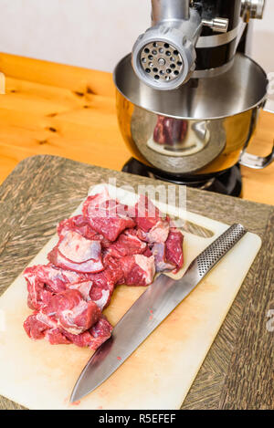Pile de couper la viande crue (Chuck) et le couteau sur une planche à découper avec hachoir à viande dans le dos. Banque D'Images