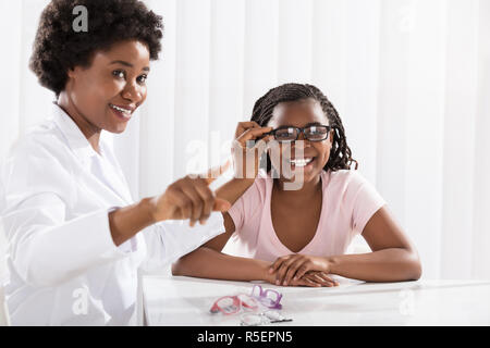 Smiling Girl Wearing Eyeglasses en face d'optométriste Banque D'Images