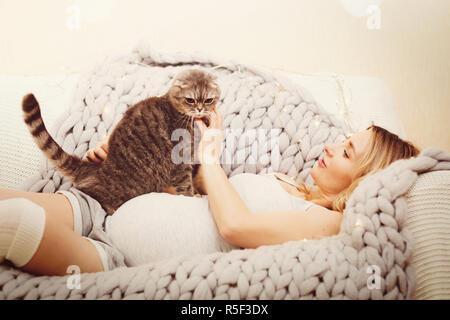 Happy pregnant woman vous détendre avec la chatte sur un canapé Banque D'Images