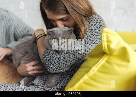 Cropped shot of woman kissing et Scottish Fold cat while sitting on couch Banque D'Images