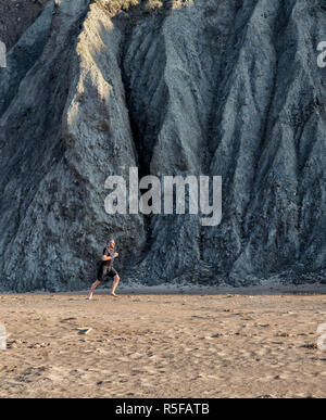 Mode de vie sain. Un homme qui court sur la plage, à côté d'immenses falaises de Mwnt, West Wales UK. Banque D'Images