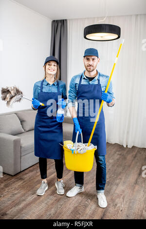 Portrait d'un jeune couple comme les nettoyeurs professionnels en uniforme bleu avec des outils de nettoyage dans l'appartement Banque D'Images