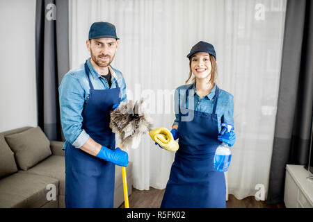 Portrait d'un jeune couple comme les nettoyeurs professionnels en uniforme bleu avec des outils de nettoyage dans l'appartement Banque D'Images