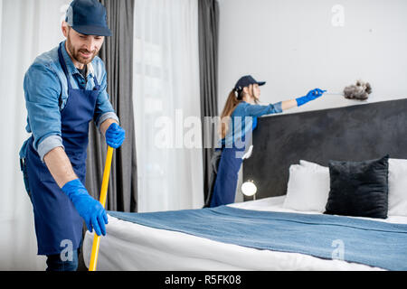 Les nettoyeurs professionnels en uniforme lave-de-chaussée et d'essuyer la poussière sur les meubles dans la chambre d'hôtel ou un appartement une chambre. Le concept de service de nettoyage Banque D'Images