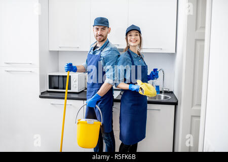 Portrait d'un couple comme les nettoyeurs professionnels en uniforme se tenant ensemble avec des outils de nettoyage à l'intérieur Banque D'Images