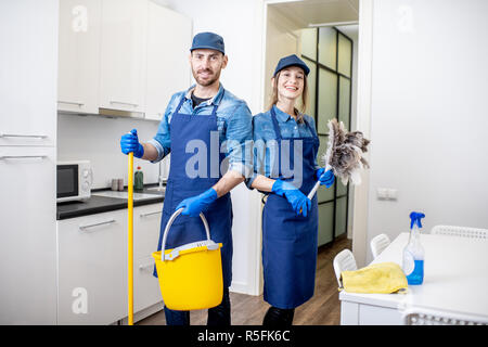 Portrait d'un couple comme les nettoyeurs professionnels en uniforme se tenant ensemble avec des outils de nettoyage à l'intérieur Banque D'Images