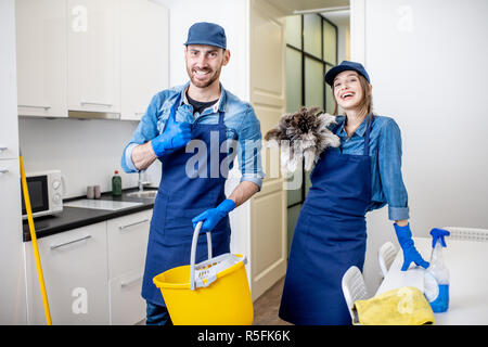 Portrait d'un couple comme les nettoyeurs professionnels en uniforme se tenant ensemble avec des outils de nettoyage à l'intérieur Banque D'Images