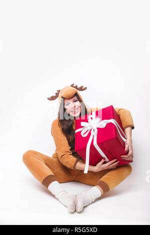 Kigurumi pyjama deer. Jolie jeune femme en pyjama assis avec big red présent fort et s'amuser sur fond blanc . Banque D'Images