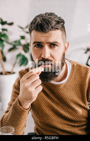 Portrait d'un homme barbu à la caméra et à la prise de comprimé d'une maladie Banque D'Images