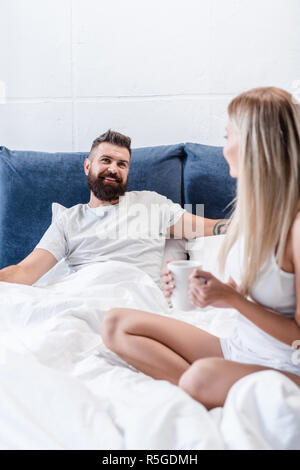 Couple heureux de parler et de boire du café au lit au matin Banque D'Images