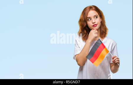 Belle Jeune femme tenant un drapeau de l'Allemagne sur fond isolé visage sérieux de penser à question, idée très confus Banque D'Images