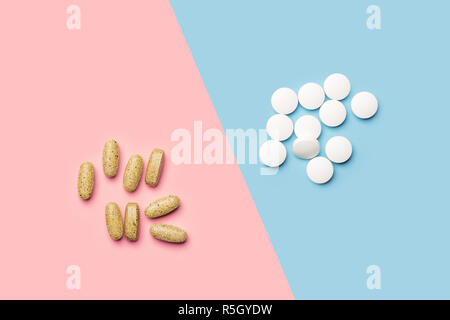Un tas de pilules blanches et un tas de vitamines jaune sur fond rose et bleu vif tourné avec studio light from above Banque D'Images