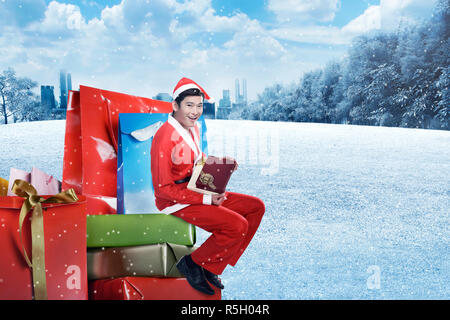 Young Asian man in santa costume s'asseoir sur la boîte-cadeau Banque D'Images
