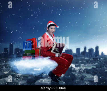 Jeune homme asiatique en costume père noël assis sur le nuage Banque D'Images