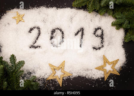2019 écrit dans la neige sur fond noir décoré avec des branches vertes et étoiles d'or Banque D'Images