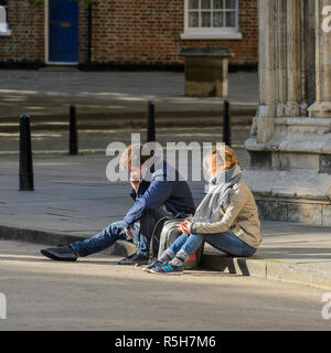 Young adult couple (mâle et femelle) assis ensemble dans soleil sur la chaussée, que l'homme fait appel - par York Minster , North Yorkshire, Angleterre, Royaume-Uni. Banque D'Images