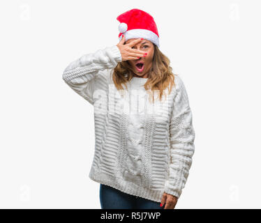 L'âge moyen senior hispanic woman wearing christmas hat sur fond isolé avec des pics de shock couvrant le visage et les yeux avec la main, à la fin de Banque D'Images