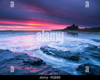 Un firey aube sur château de Bamburgh et les roches Harkness. Banque D'Images