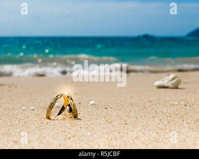 Miel, sur l'île tropicale, deux anneaux de mariage sur la plage, de sable, de ciel et l'océan en arrière-plan Banque D'Images