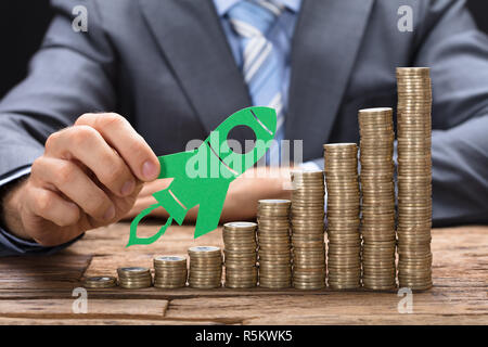 Businessman Holding Livre Vert Rocket sur pièces empilées sur la table Banque D'Images