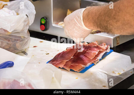 Un homme part slicing raw ham avec une machine à emballer, Croatie. Banque D'Images