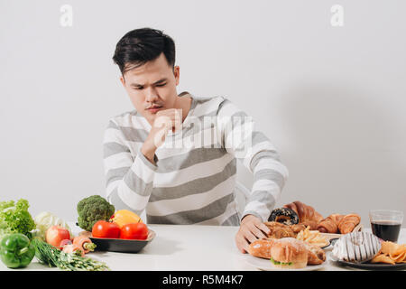 Homme avoir choix difficile entre les aliments sains et malsains Banque D'Images