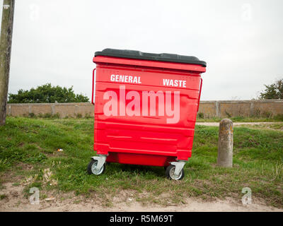 Un bac à déchets général rouge seul à l'extérieur sur l'herbe Banque D'Images