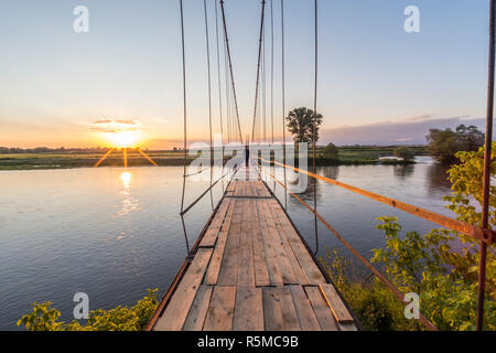 Homme marchant sur un vieux pont suspendu vers le coucher du soleil. Banque D'Images