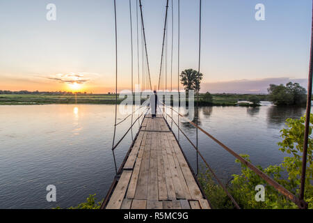 Homme marchant sur un vieux pont suspendu vers le coucher du soleil. Banque D'Images