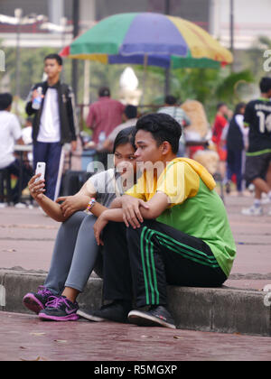 Photo horizontale des contenus, young Indonesian man posant sa tête sur l'épaule de petit ami à la recherche de téléphone cellulaire d'autoportraits pris ce jour-là. Banque D'Images