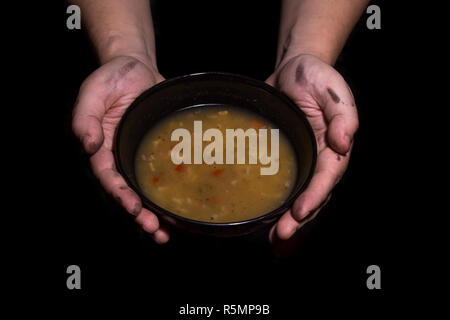 Concept de la pauvreté. L'homme avec les mains sales tenait un bol de soupe isolé sur fond noir. Banque D'Images