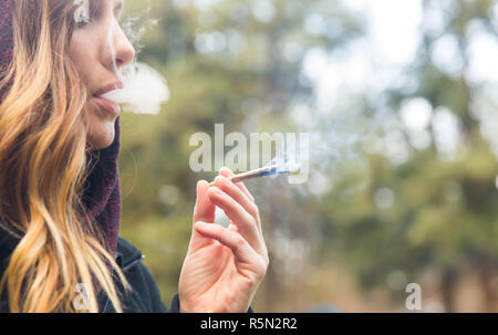 Attrayant, jeune femme blonde, fumeurs de cannabis ou de la marijuana, un joint (cigarette) à l'extérieur. Banque D'Images